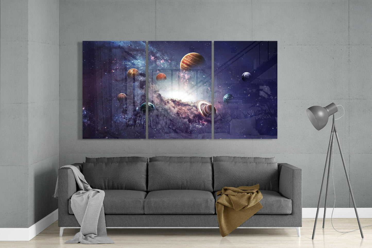 Three-panel Milky Way glass art displaying planets and galaxy in purple and gold tones mounted above gray sofa in modern living room.