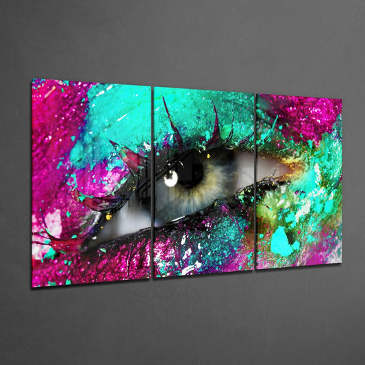 Three-panel glass wall art displaying a close-up eye with magenta, cyan, and green paint splatters and spiky protrusions.