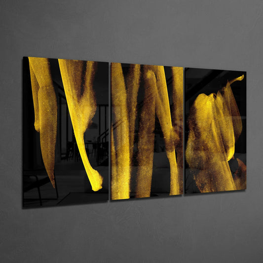 Three-panel black glass wall art with vertical gold and bronze streaked textures displayed at an angle against gray wall.