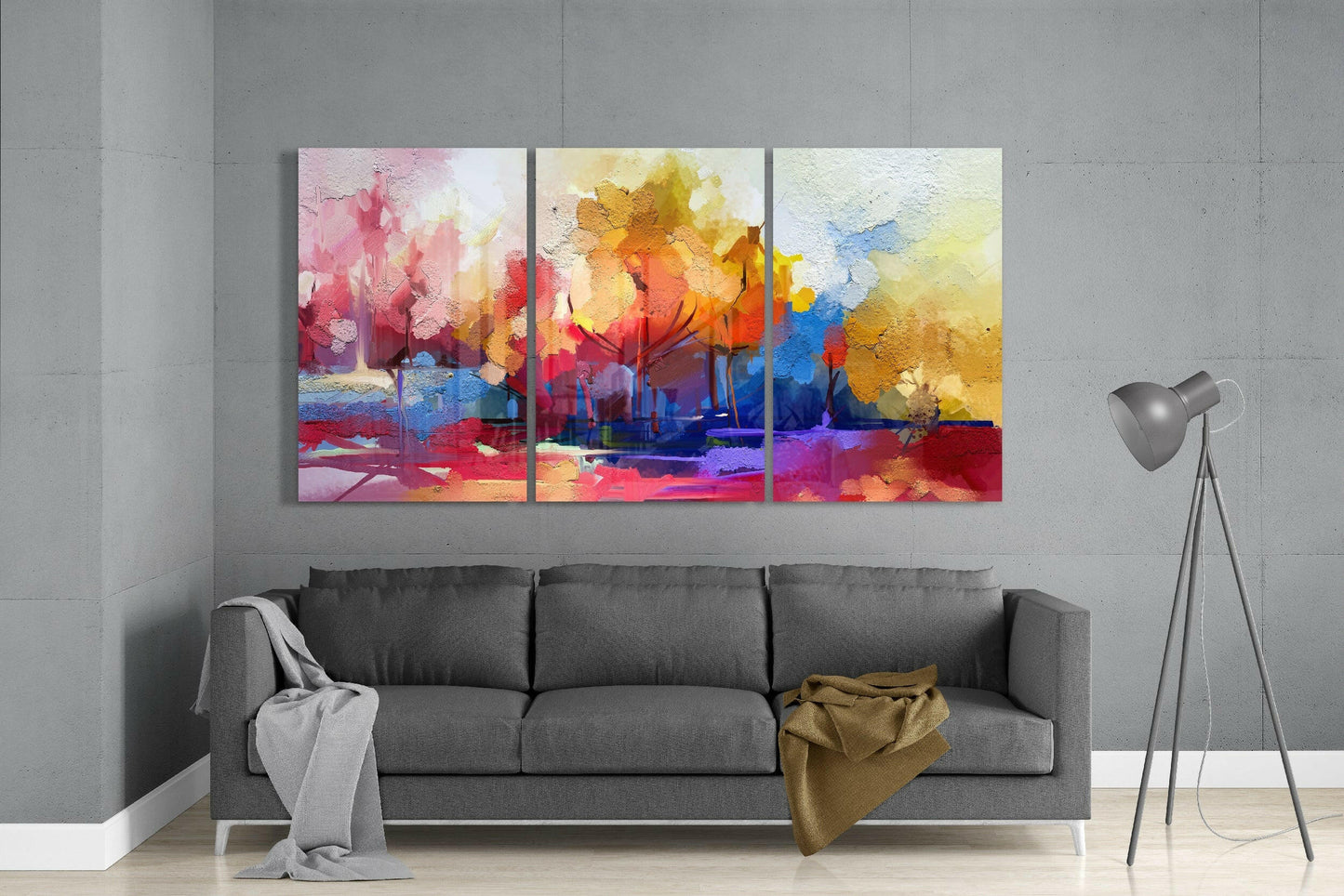 Triptych glass art panels displaying vibrant watercolor landscape with pink, yellow, orange, and blue hues above gray sofa in modern interior.