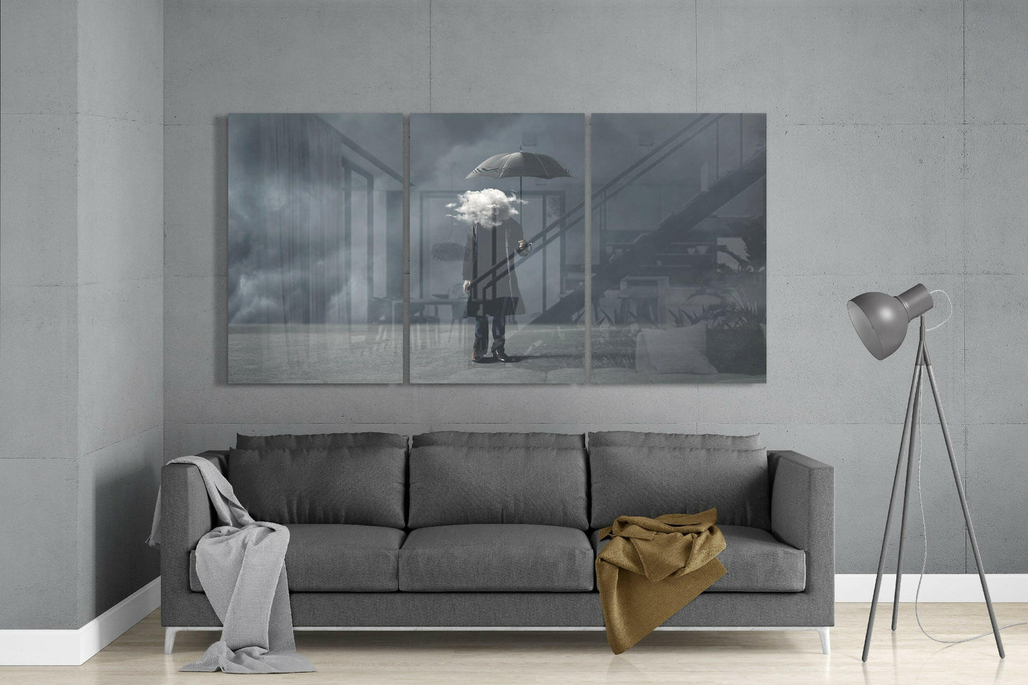 Three-panel glass art depicting a figure holding an umbrella sheltering a white cloud, displayed above a gray sofa in a minimalist living room.