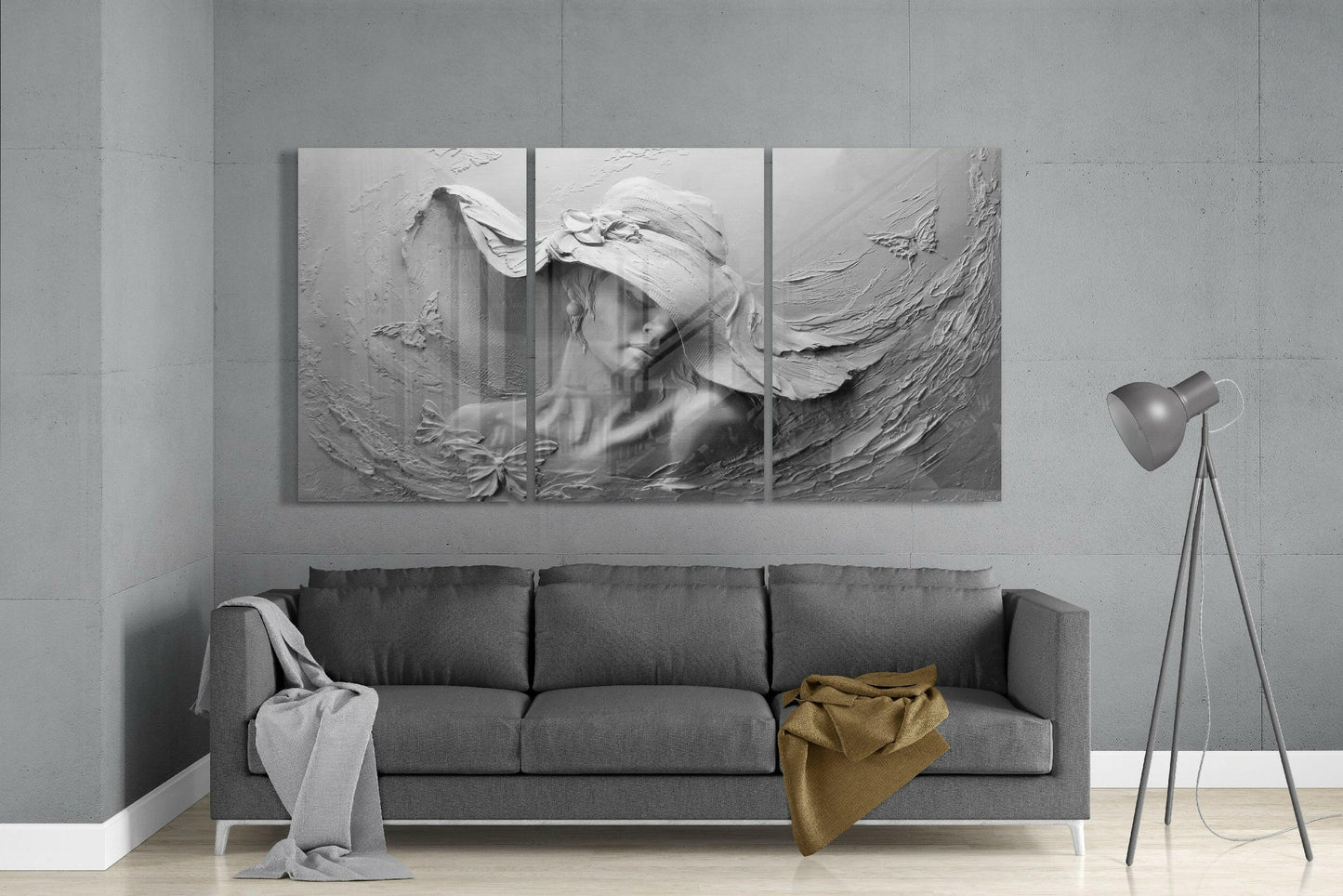 Three-panel monochromatic glass art depicting a woman's portrait with textured relief surface, displayed above gray sofa in minimalist interior.