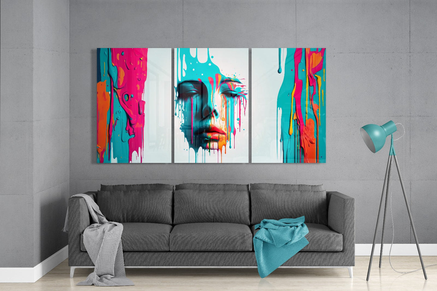 Colorful triptych glass wall art featuring a woman's face with vibrant turquoise, pink, orange, and red paint drips displayed above a gray sofa in a modern living room.