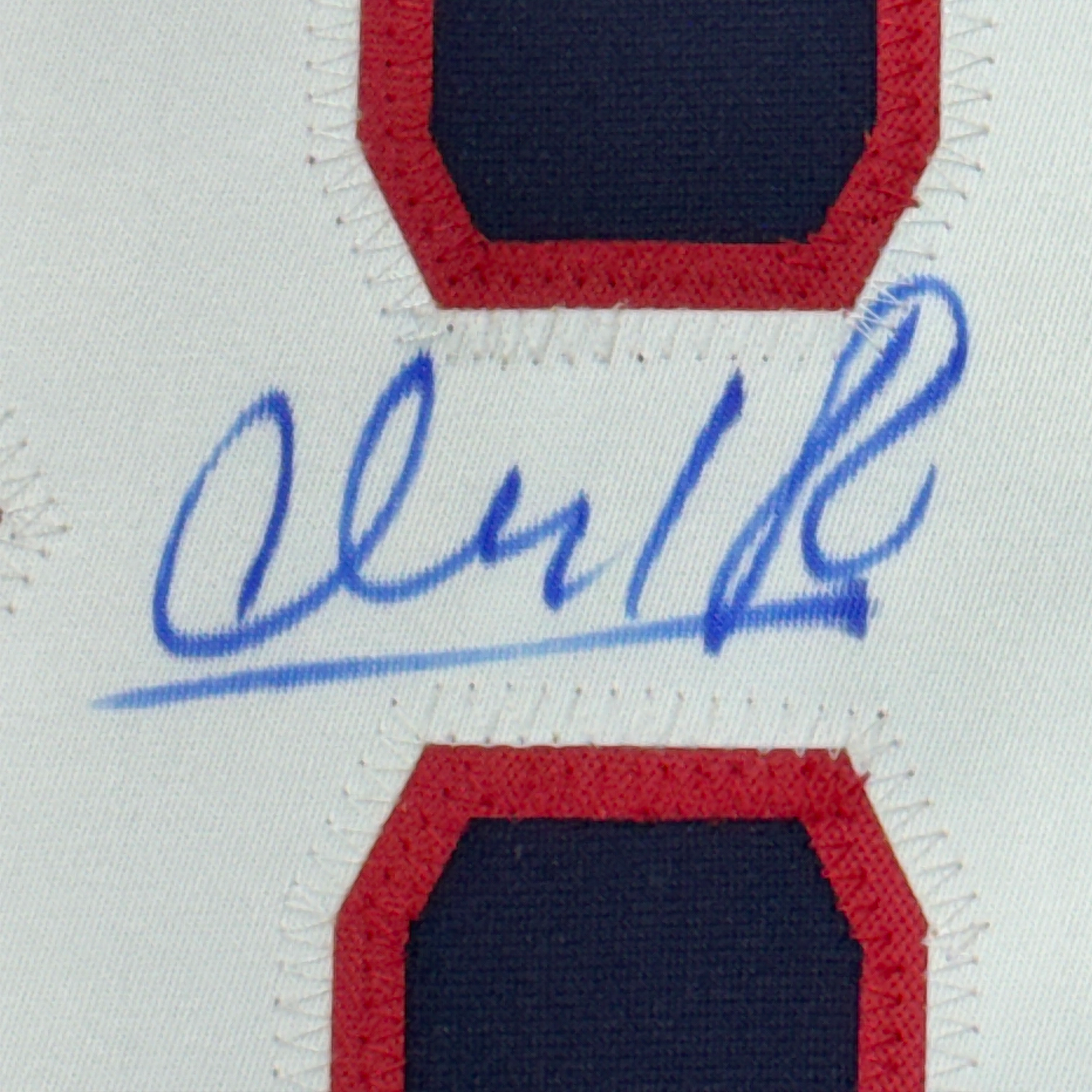 Close-up of blue autograph signature on white jersey fabric with red and navy blue striped trim visible above and below.