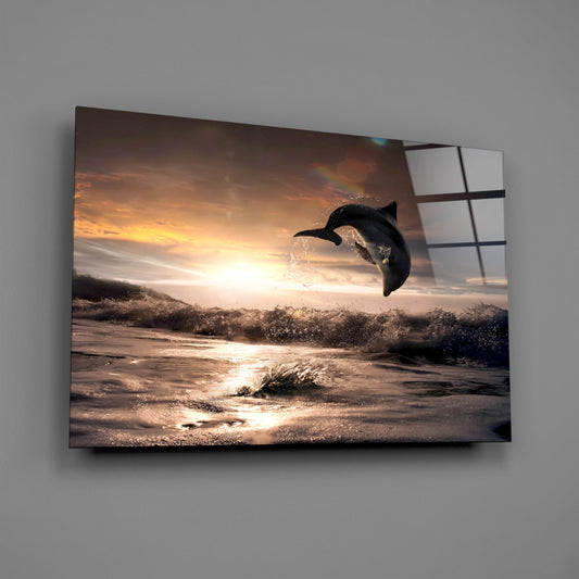 Glass wall art panel displaying a dolphin leaping above ocean waves at golden sunset, mounted at an angle against gray wall.
