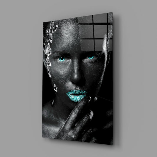 Angled view of glass wall art depicting a grayscale face with turquoise eyes and lips, mounted on gray wall.