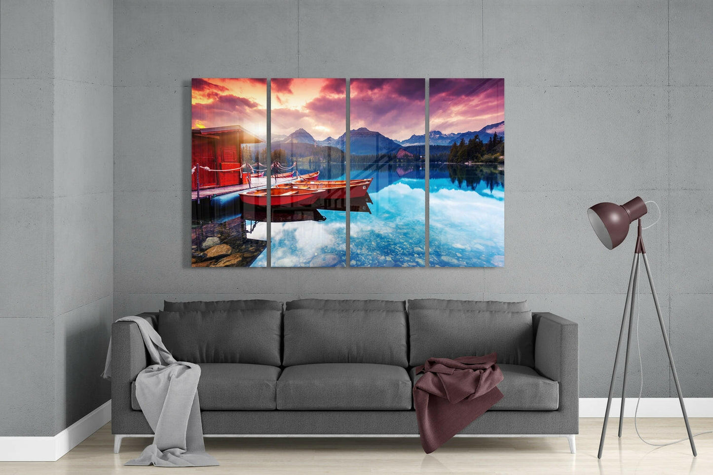 Four-panel glass wall art displaying red boats on a turquoise alpine lake at sunset, hung above a gray sofa in a modern living room.