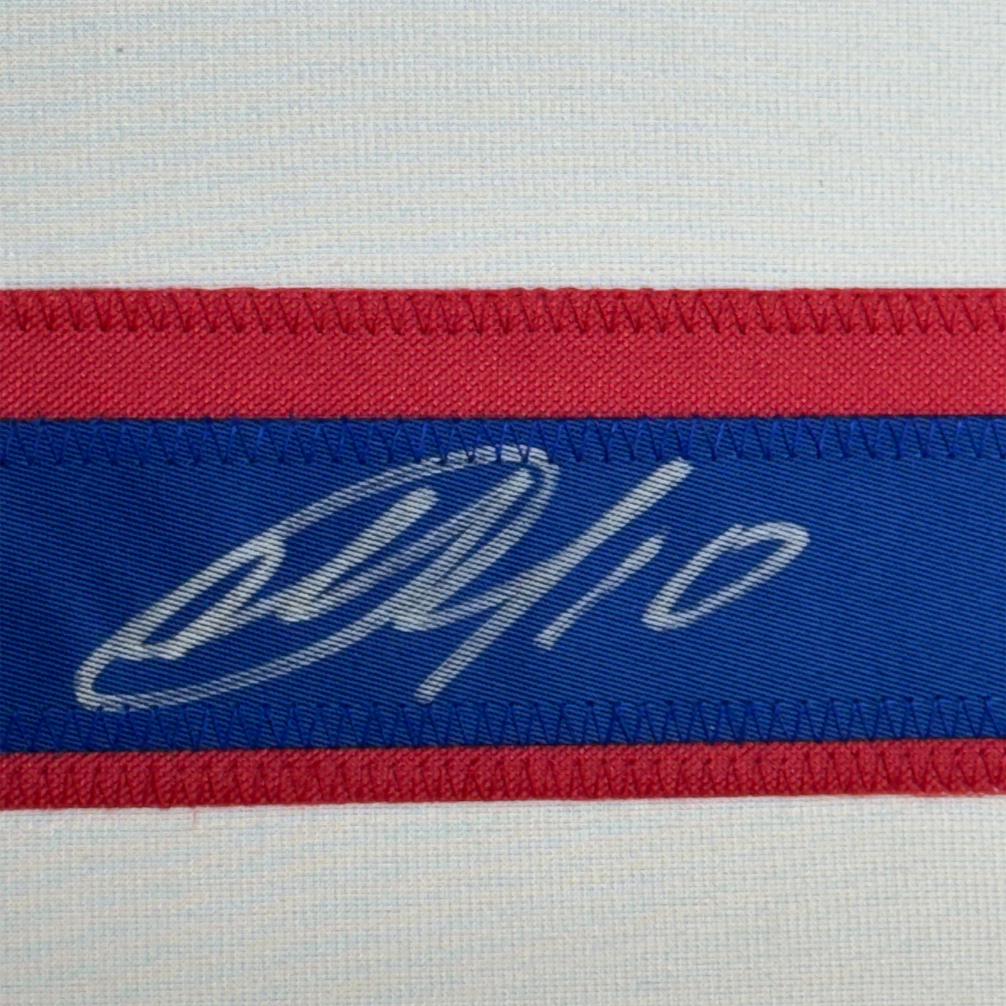 Close-up of striped ribbon featuring a handwritten signature on blue band between red stripes.