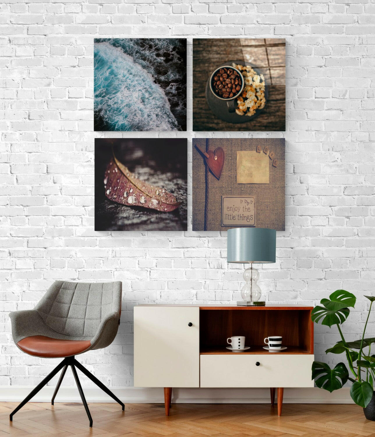 Four-panel glass wall art display mounted on white brick, showing ocean waves, food bowl, decorative shoe, and motivational "enjoy the little things" text on brown fabric background.