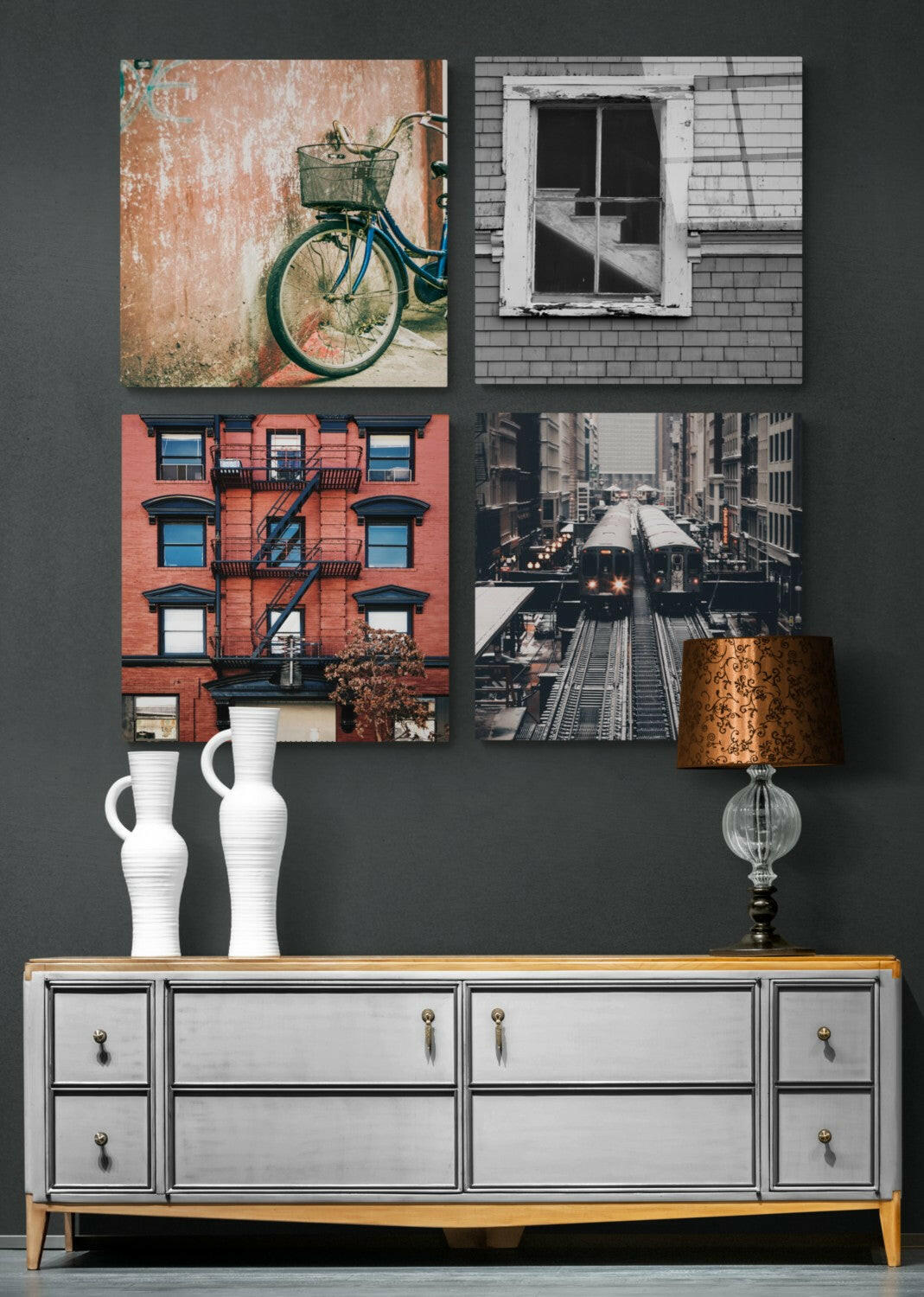 Four square glass panels mounted on gray wall above white dresser with wood top, displaying urban photographs of bicycle, window, building facade, and subway train.