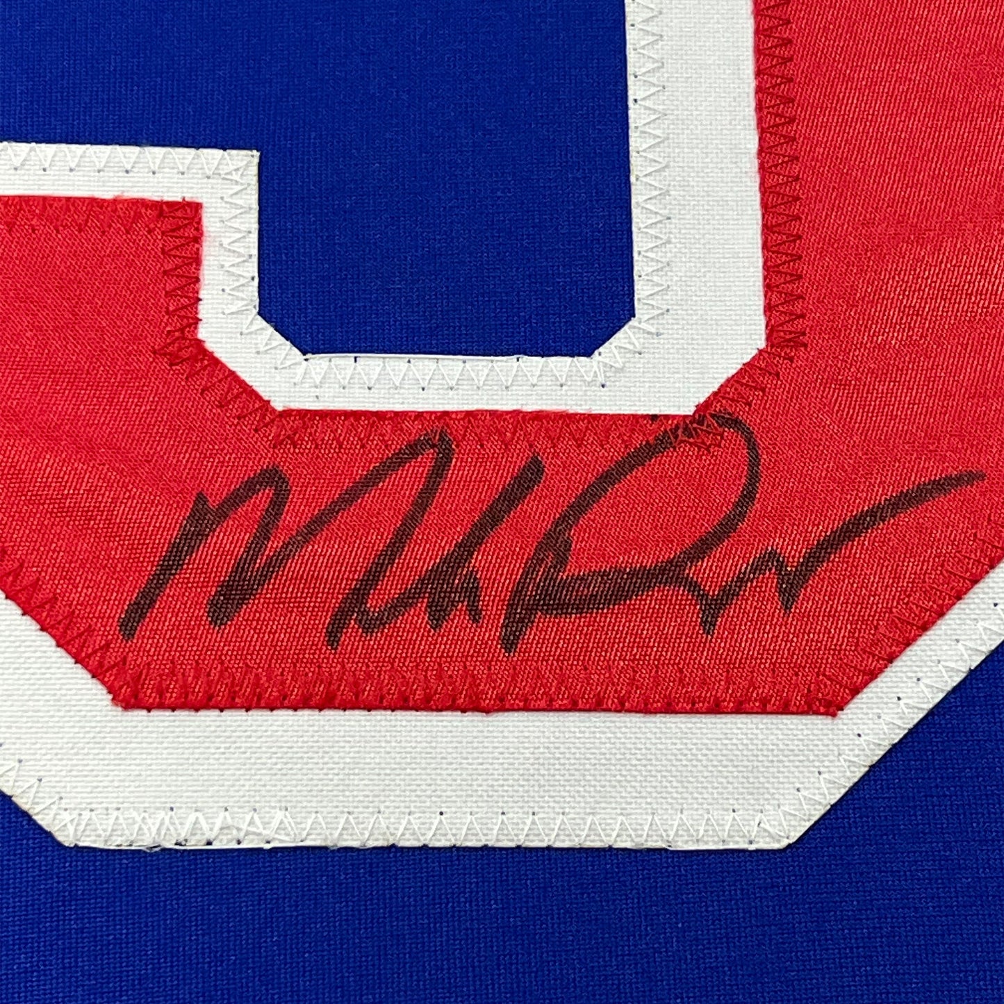 Close-up of autographed red chest stripe on blue New York Rangers hockey jersey showing handwritten signature.