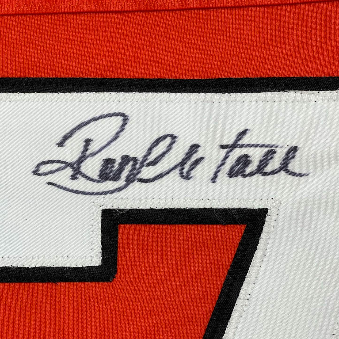 Close-up of handwritten signature "Ron Hextall" in blue ink on white jersey label with red and black fabric visible.