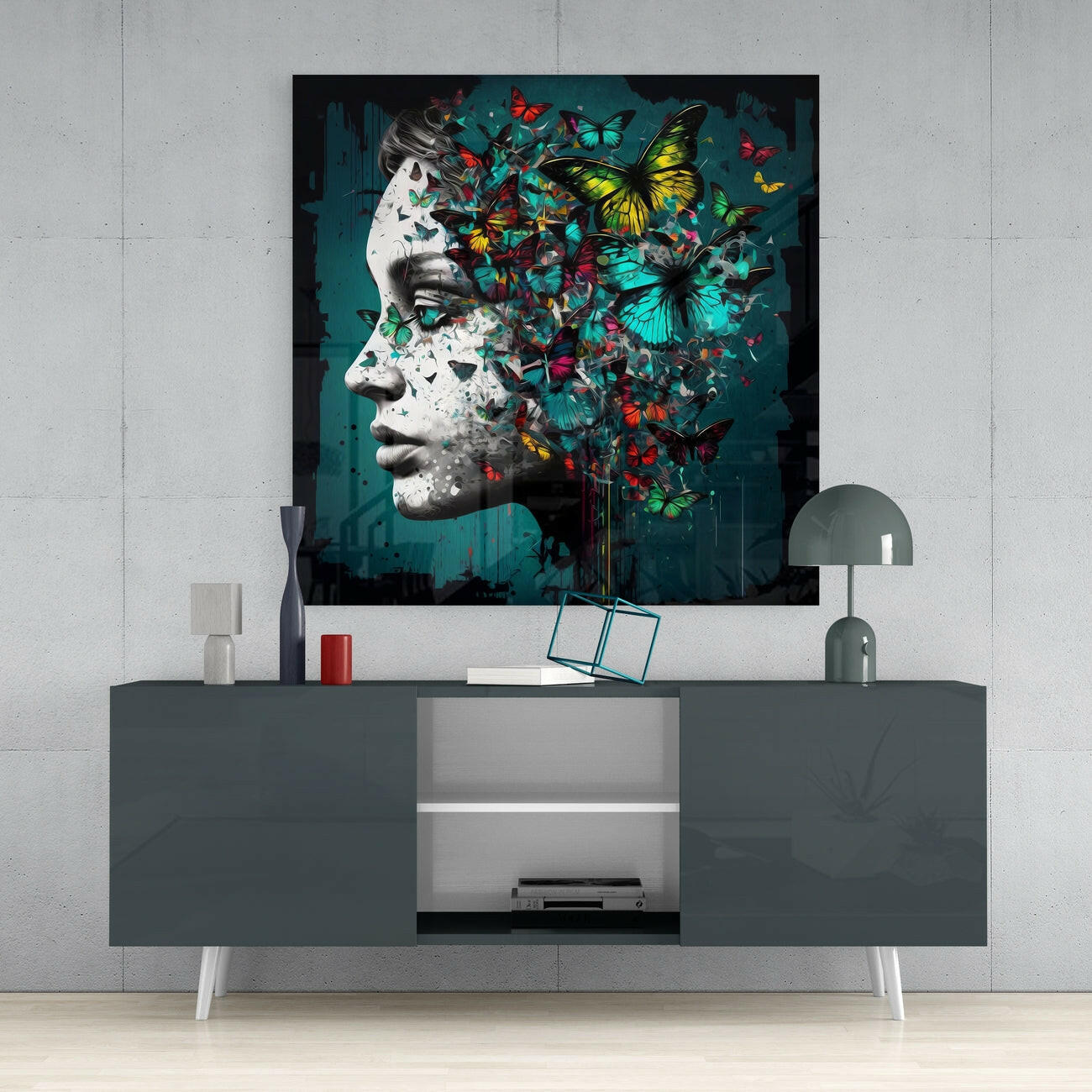 Glass wall art depicting a monochrome sculptural profile with colorful butterflies dispersing across teal background, displayed above gray media console.
