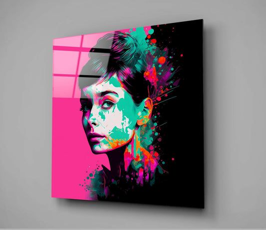 Angled view of a glass wall art panel featuring a neon pink and black portrait with colorful paint splatter effects in cyan, magenta, and orange tones.