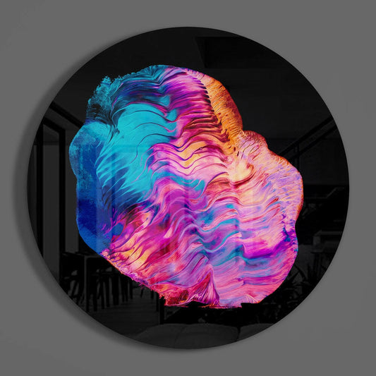 Circular glass wall art with vibrant neon blue, pink, magenta, and golden yellow fluid waves swirled across black background, mounted on gray wall.
