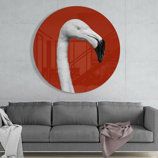 Circular red glass wall art featuring a white flamingo's head and neck in profile, displayed above a gray sofa in a modern interior.