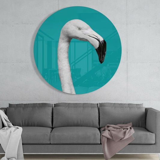 Circular teal glass wall art featuring white flamingo head with black beak mounted above gray sofa in modern interior setting.