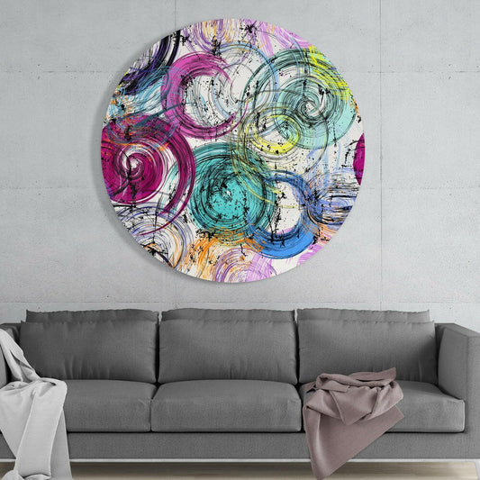 Circular glass wall art with swirling pink, teal, yellow, and blue ink patterns hanging above gray sofa in modern interior.