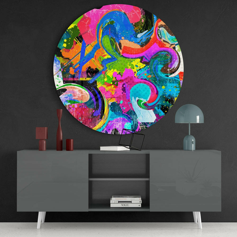 Vibrant circular glass wall art displaying colorful abstract swirls in pink, blue, green, and yellow mounted above gray console table with accessories.