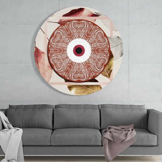 Terracotta ornate eye disc with intricate white line patterns and pink iris mounted on cream background with pressed leaves, displayed above gray sofa.