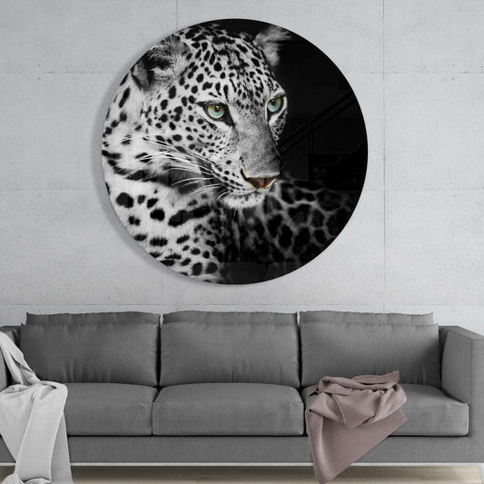 Circular black and white glass wall art featuring a leopard's face with striking green eyes, displayed above a gray sofa in a modern interior.
