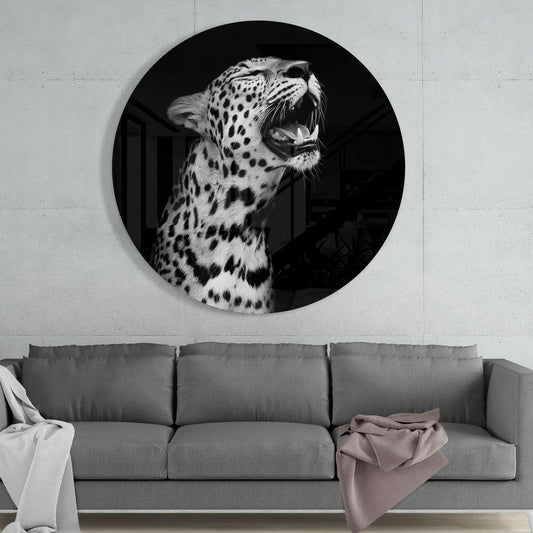 Round black and white glass wall art depicting a yawning leopard mounted above a gray sofa in a modern interior.
