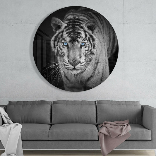 Circular black and white tiger portrait with striking blue eyes mounted on white wall above gray sofa.
