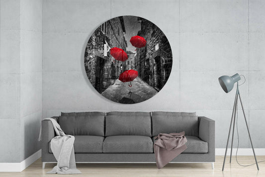 Circular glass wall art displaying black and white street scene with three red umbrellas, mounted above gray sofa in modern living room.