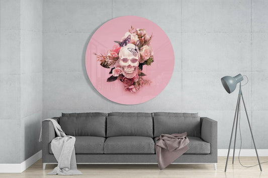 Pink circular glass wall art featuring a skull with pink roses and butterflies, displayed above a gray sofa in a modern living room.