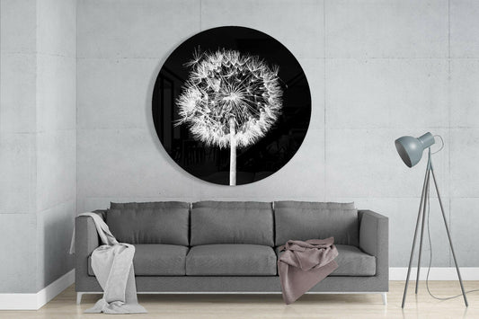 Round black glass wall art with white backlit dandelion design displayed above gray sofa in minimalist living room.