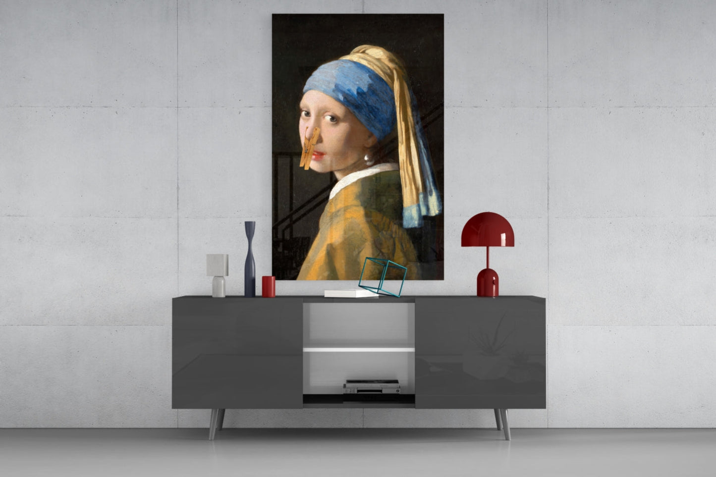 Modern living room styled display featuring Girl with a Pearl Earring portrait on wall above gray console table with red lamp and decorative objects.