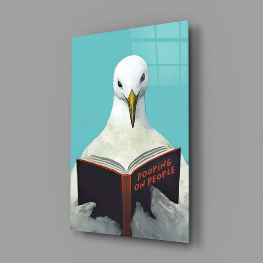 Three-quarter view of glass wall art showing white seagull reading black book titled "Pooping on People" against turquoise background.