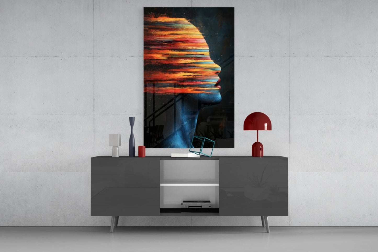 Modern living room display featuring colorful profile silhouette glass art mounted above gray media console with red lamp and accessories.