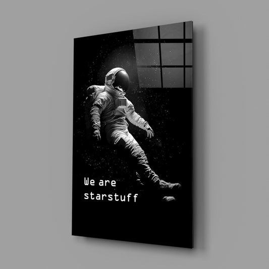 Angled view of black glass wall art featuring a white astronaut floating in space with "We are starstuff" text, displayed against gray wall.