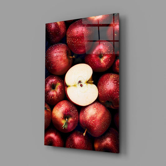 Glass wall art panel displaying fresh red apples with water droplets surrounding a sliced apple half, angled perspective view.