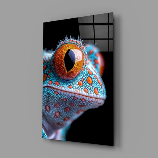 Close-up side profile of a colorful reptile eye with golden iris and vertical pupil, turquoise and orange textured scales, printed on black glass panel.