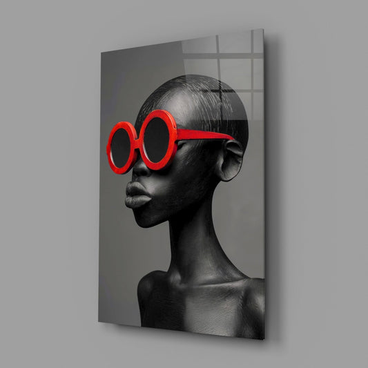 Black and white sculptural portrait wearing oversized red circular sunglasses, displayed as a tilted glass wall panel against gray background.