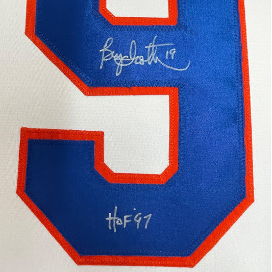 Close-up of blue hockey jersey back showing white number outline with signatures "Bryan Trottier 19" and "HOF 91" in silver ink.