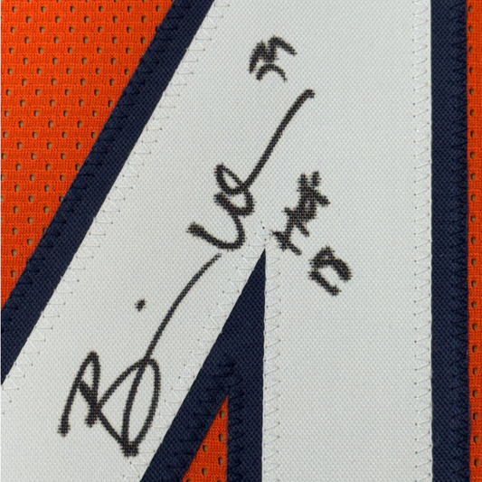 Close-up of a white jersey panel with navy trim and orange mesh, showing part of a black marker signature.