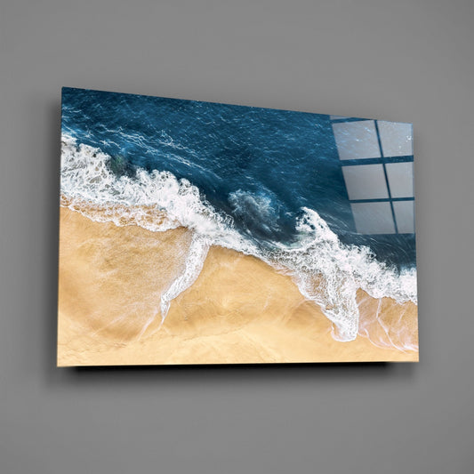 Aerial view of sandy beach with white-capped waves on glass wall art mounted on gray wall, showing grid pattern overlay on right edge.