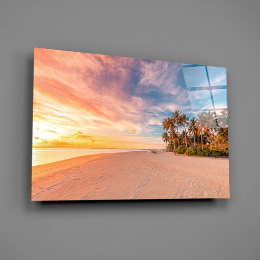 Glass wall art displaying a tropical beach sunset with palm trees, golden sky, and sandy shore mounted on gray wall.