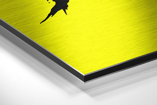 Close-up angled view of yellow brushed aluminum dibond panel with black silhouette graphic and beveled edge detail.
