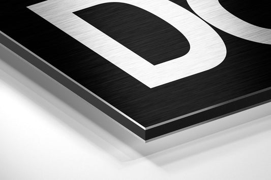 Close-up angled view of brushed aluminum dibond wall art with black and white geometric stripe design and metallic silver edges.
