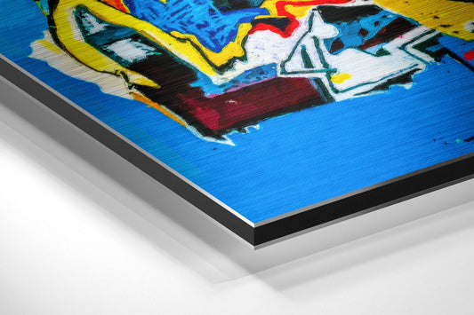 Angled 3D perspective view of brushed aluminum dibond wall art featuring blue background with vibrant yellow, red, white, and black abstract face design.