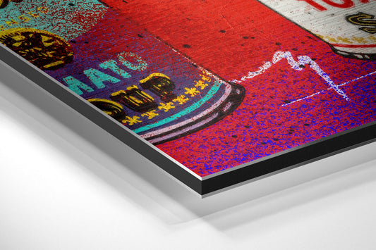 Angled close-up of vibrant pop art print on brushed aluminum dibond showing colorful stacked soup cans with red, blue, yellow, and turquoise hues.