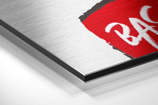Close-up angled view of brushed aluminum dibond panel edge showing layered construction with red tribal face design and white symbols visible on surface.