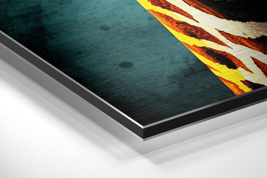 Close-up angled view of layered aluminum dibond print showing teal brushed surface with yellow and orange flame-like design along right edge.