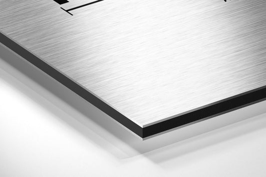Close-up angled view of brushed aluminum Dibond panel edge showing layered white surface and black trim against white background.
