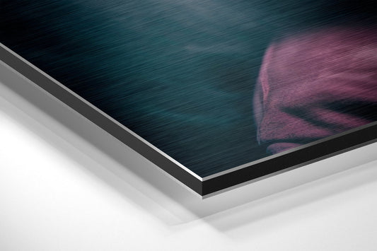 Close-up angled view of brushed aluminum Dibond print edge showing layered material construction with teal and pink hooded figure visible on surface.