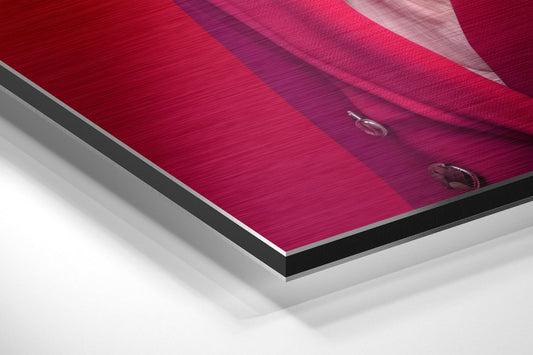 Close-up angled view of layered aluminum dibond print showing crimson and magenta fabric texture with metallic edge detail against white background.